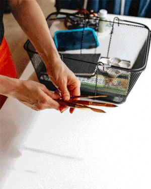 A gif of a white woman's hands placing red-handled paintbrushes into a shopping basket at a Vermont art shop.