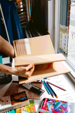 A colorful gif of a white person's hands flipping through a brown toned sketchbook in a Vermont art store.