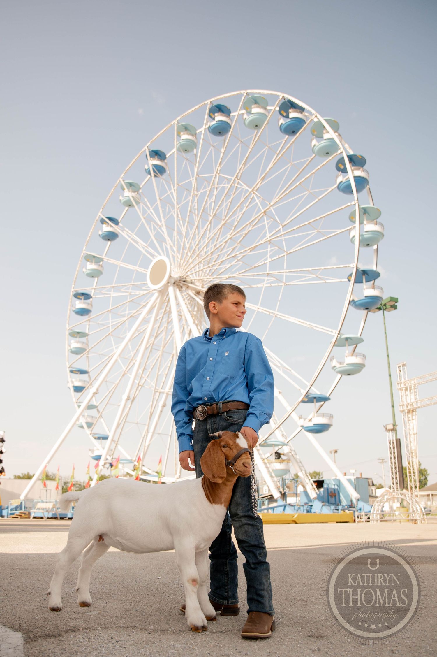 Boy in blue shirt leads a goat at a county fair entrance with Welcome to the Fair sign backdrop.