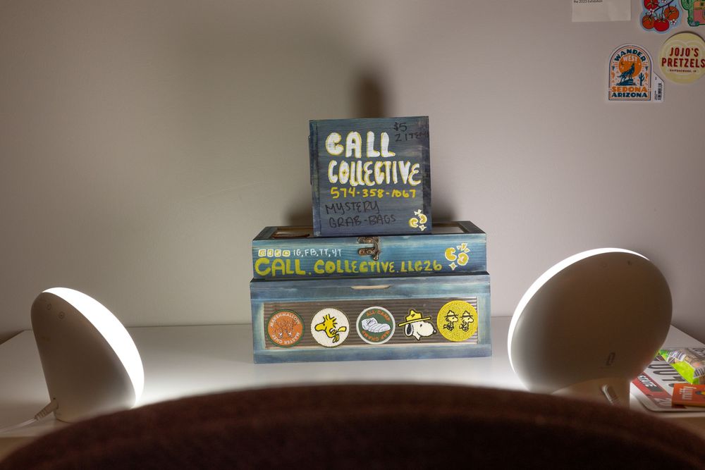 Two stacked Call Collective board game boxes displayed on a white shelf between two white speakers.