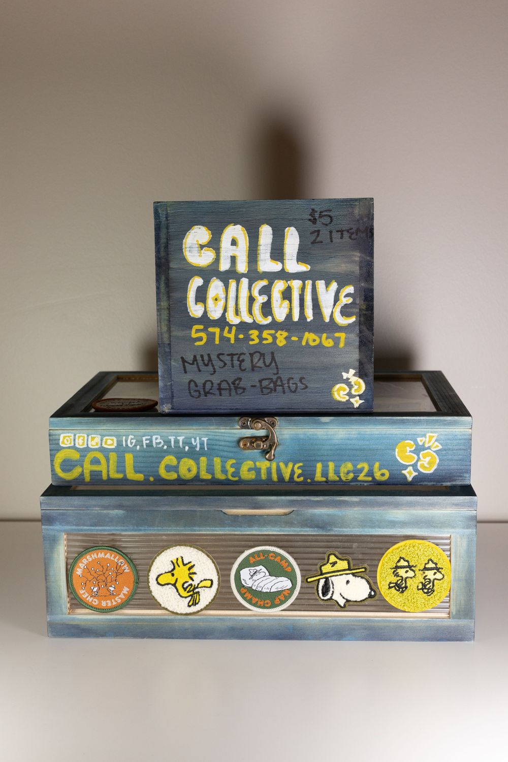 Painted wooden boxes advertising Call Collective LLC with phone number 574-358-1067, mystery grab bags, and Snoopy character stickers.