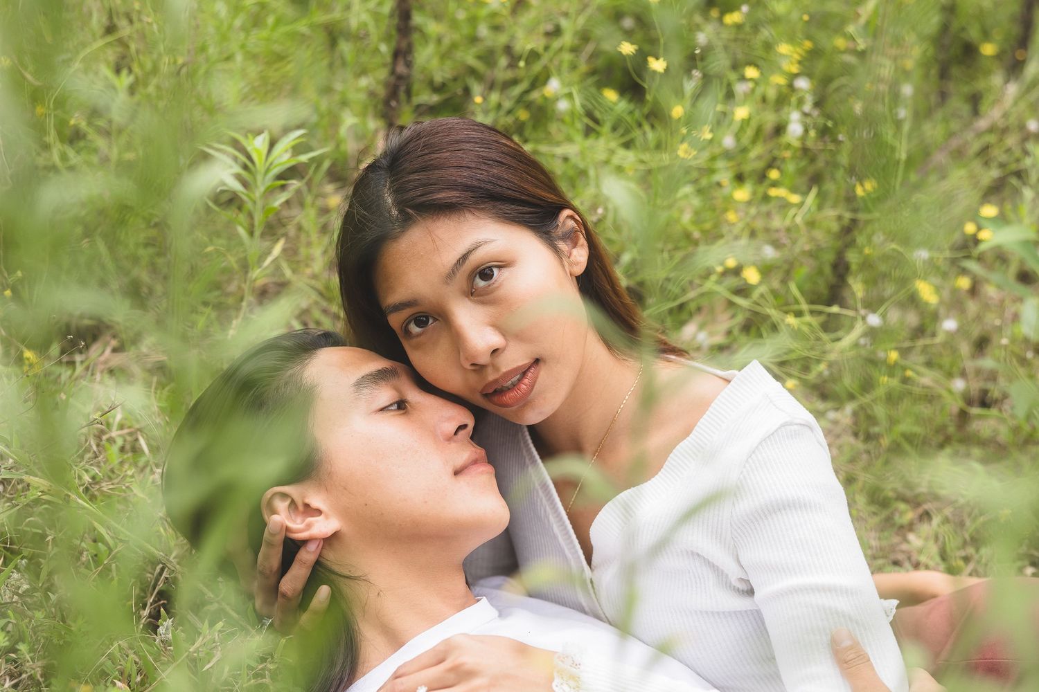 Two young Asian women sharing a tender moment together surrounded by lush green foliage.