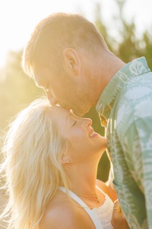Romantic couple almost kissing in warm golden sunlight with soft bokeh background outdoors.