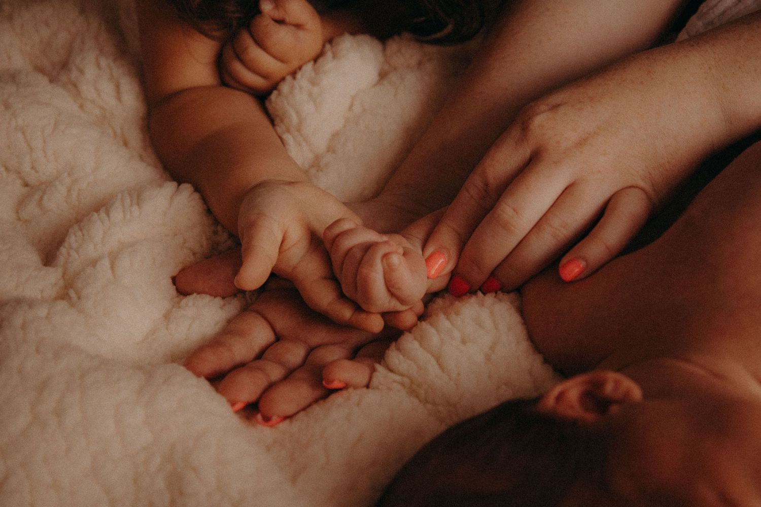 Tender newborn baby hands held by parents on soft white blanket.