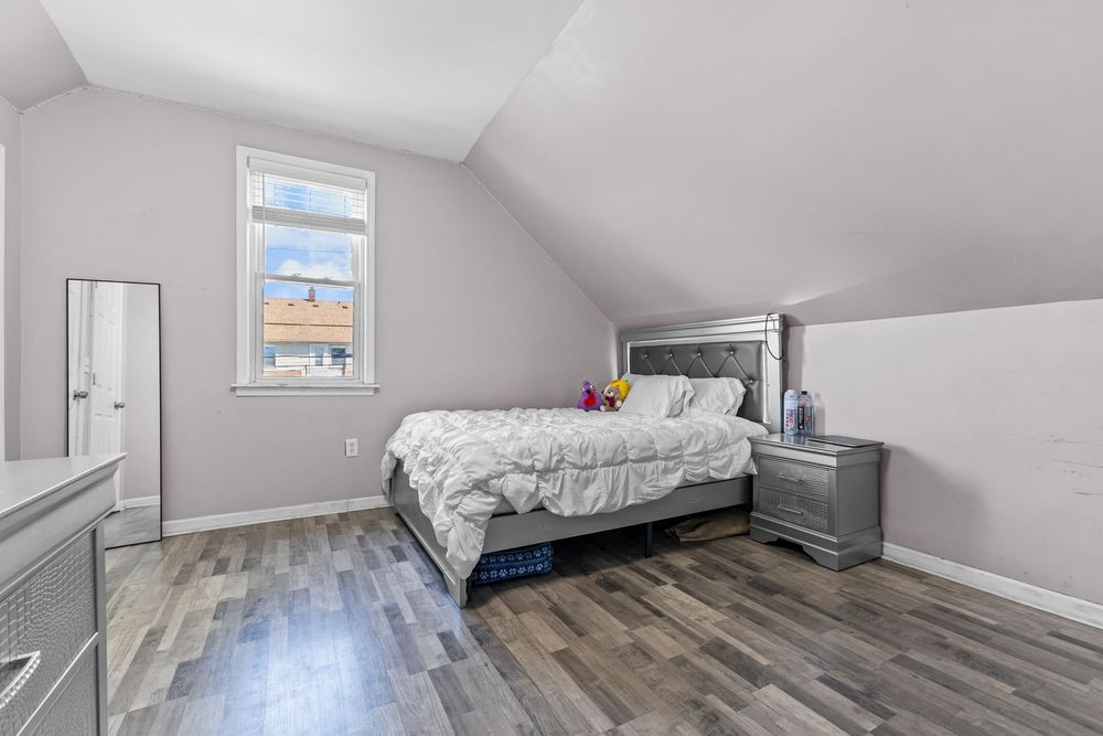 Attic bedroom with vaulted ceilings, dark hardwood floors, a bed with white bedding, and a window.