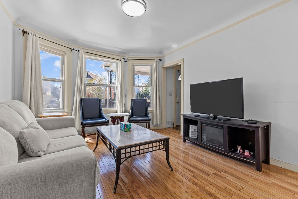Bright living room with hardwood floors large windows gray sofa fireplace console and flat screen TV.
