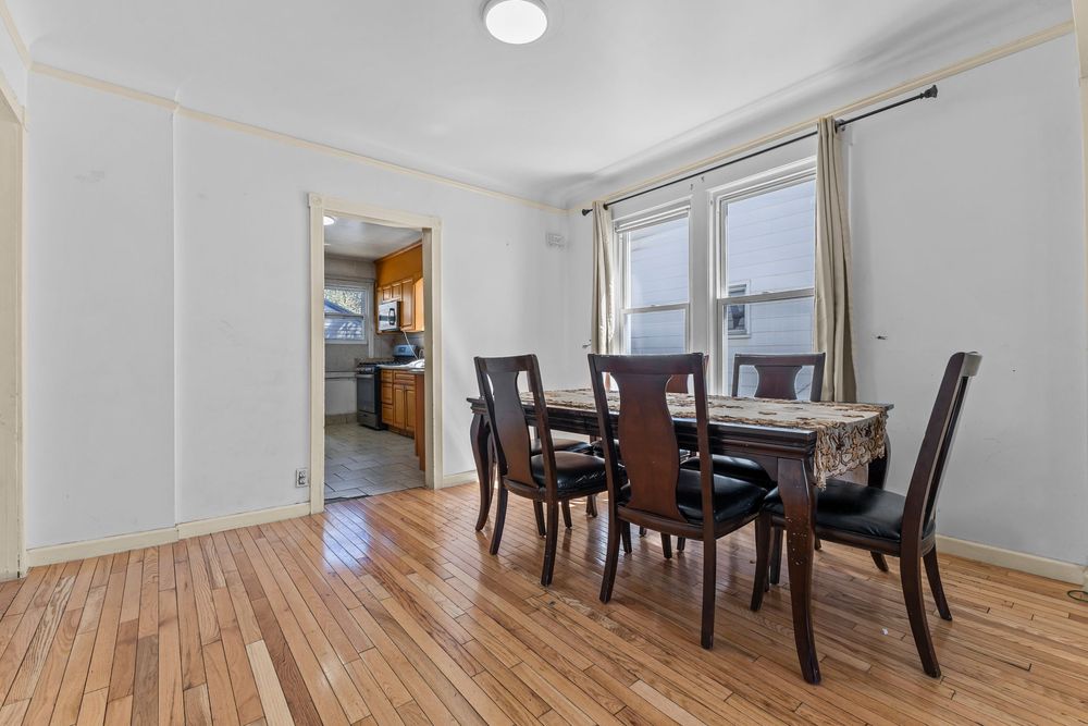 Dining room with hardwood floors dark wood table and chairs large window and view into kitchen.