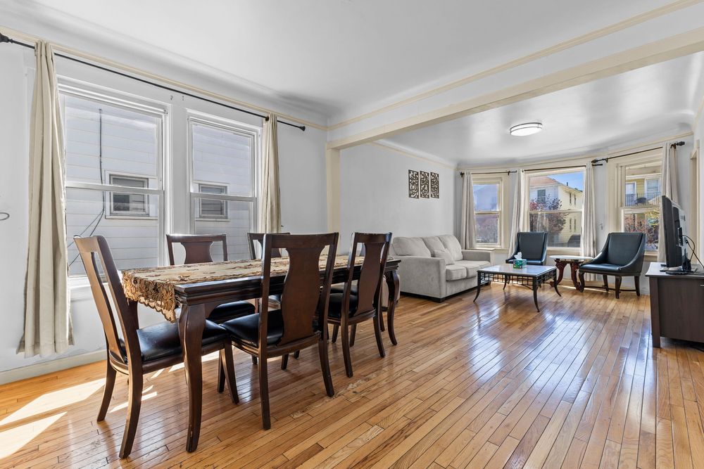 Open dining and living room with hardwood floors dark dining set multiple windows and natural light.