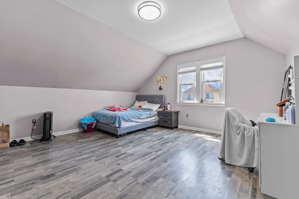 Spacious attic bedroom with vaulted ceilings, hardwood floors, a bed, and a window allowing natural light.