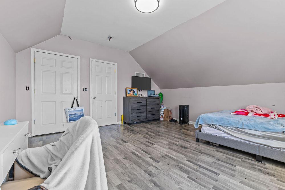 Attic bedroom with sloped ceilings, hardwood floors, a dresser, and a bed with white bedding.