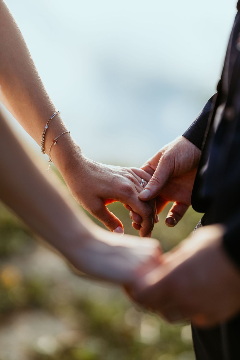 Close-up of bride and groom holding hands, bride wearing a delicate bracelet and wedding ring.