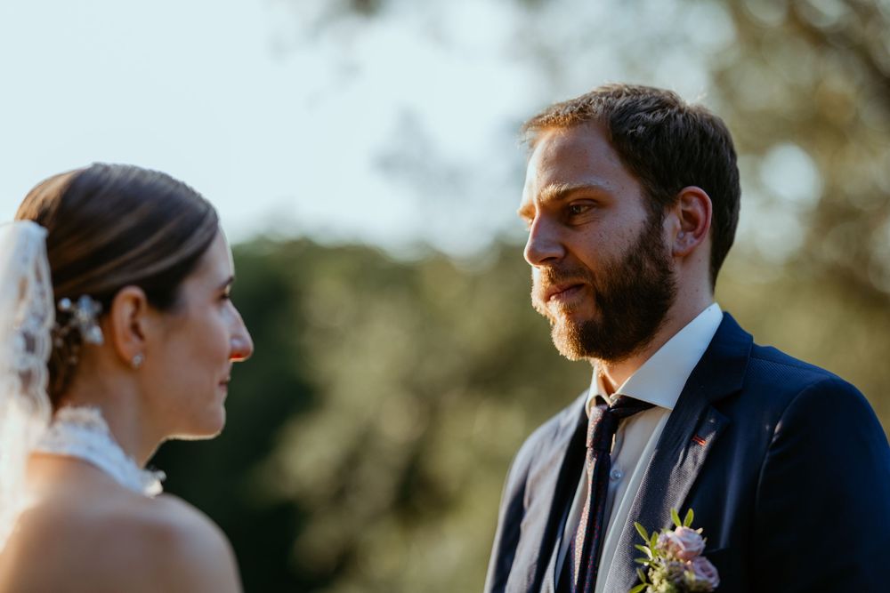 Bride and bearded groom in navy suit sharing an intimate gaze outdoors at golden hour.