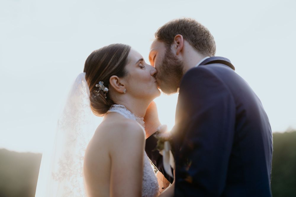 Bride and groom sharing a romantic kiss at sunset during their outdoor wedding.