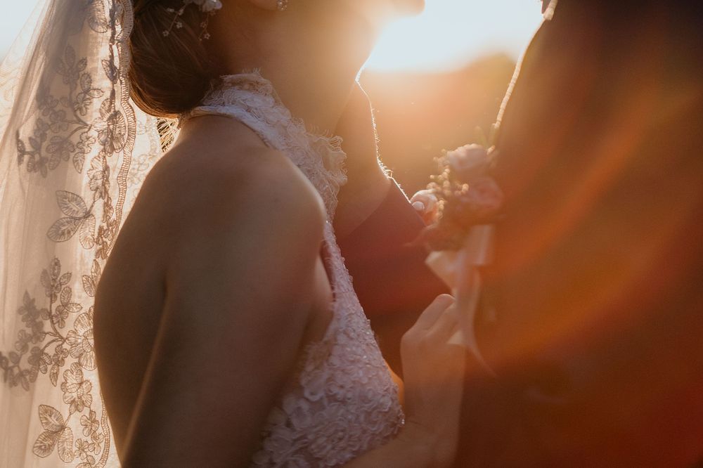 Close-up of bride in lace wedding dress with veil glowing in warm sunset light.