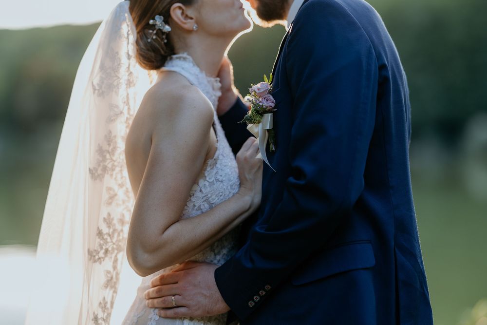 Bride and groom sharing a tender kiss outdoors near a lake at sunset.