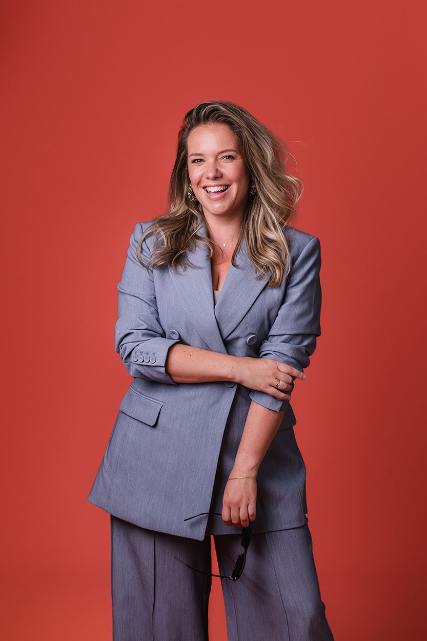 Vrouwelijke ondernemer in de studio die lachend kijkt met een oranje achtergrond. Een lichte luchtige vrolijke zakelijke portretshoot.