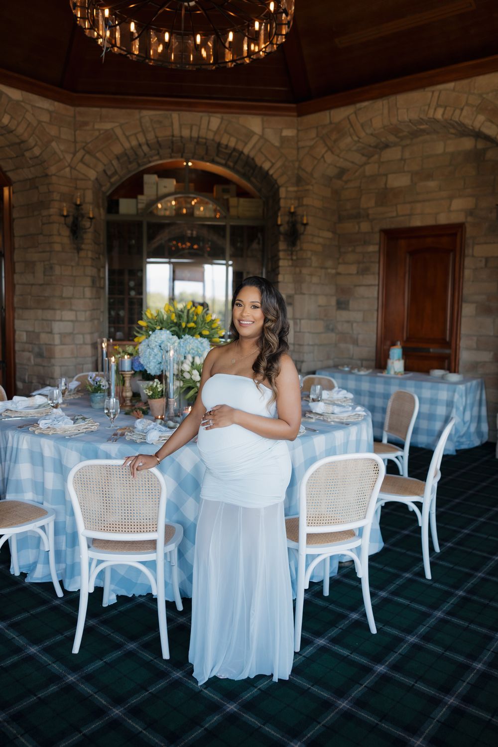 Pregnant woman in white dress stands at elegantly decorated baby shower table indoors.