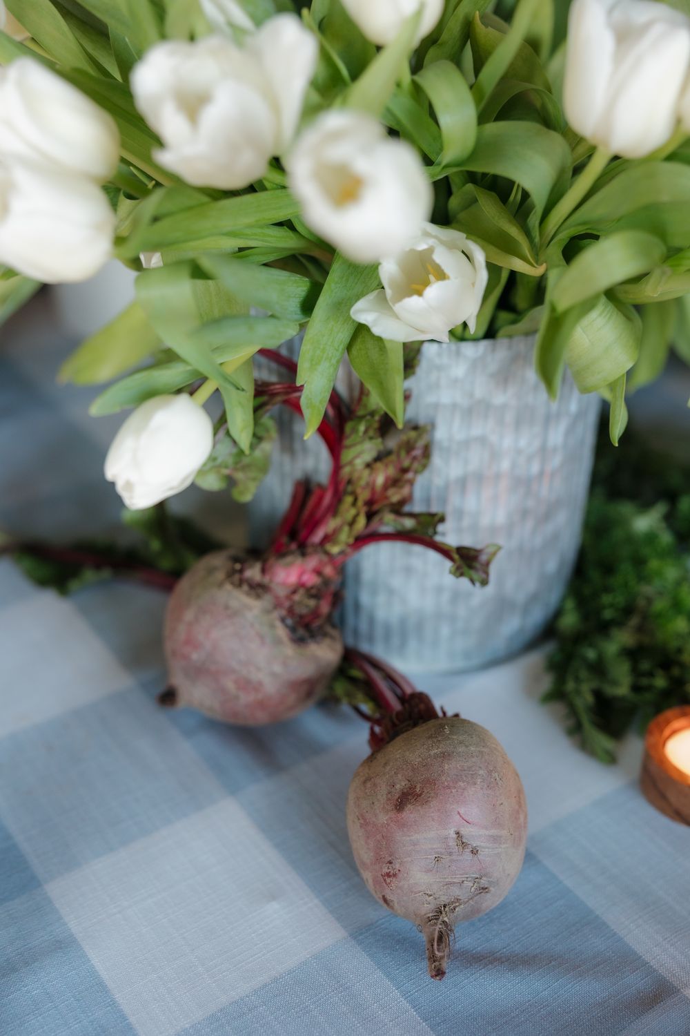 Fresh beets and white tulips in a blue vase on a gingham tablecloth for an elegant spring table setting.