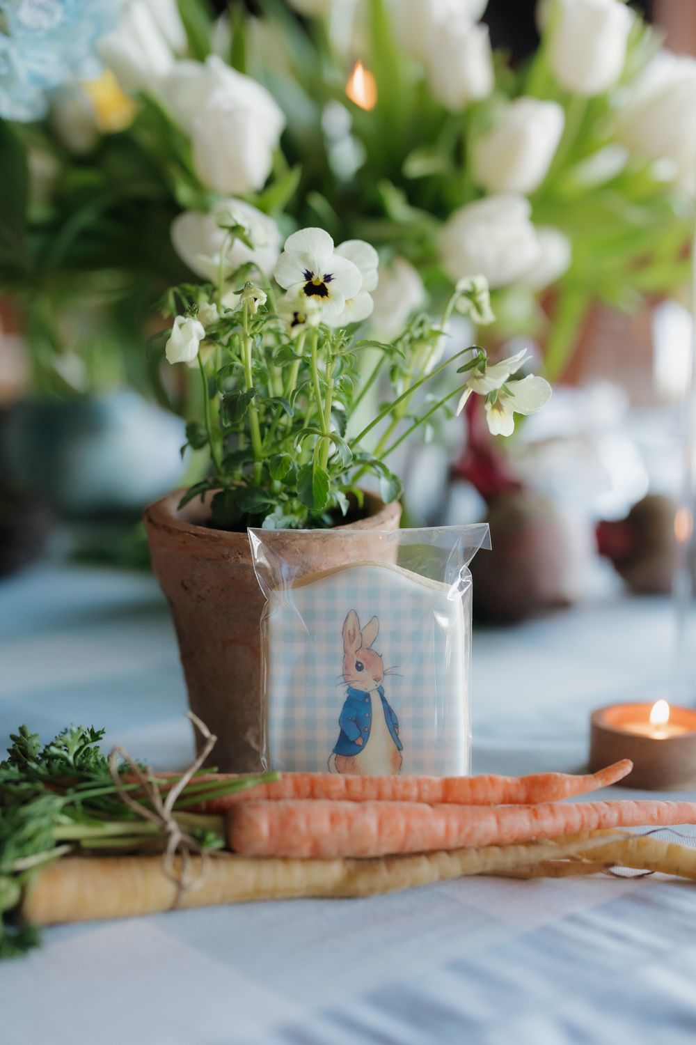 Peter Rabbit themed table decor with white tulips, carrots, and cookie favor on blue gingham tablecloth.