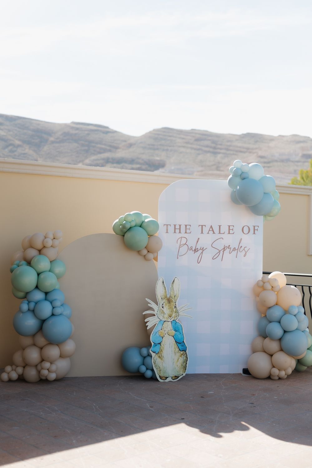 Peter Rabbit baby shower backdrop with balloon garland in blue, sage, and nude tones, reading The Tale of Baby Sproles.