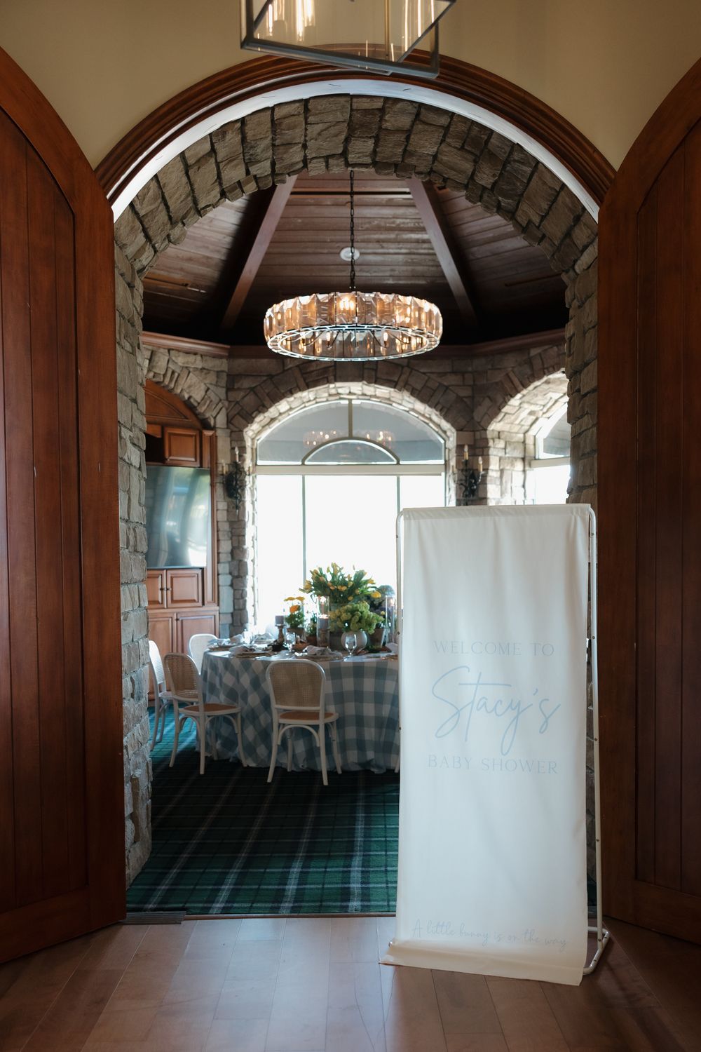 Elegant baby shower venue with stone arched doorway, chandelier, and personalized Stacy's banner at entrance.
