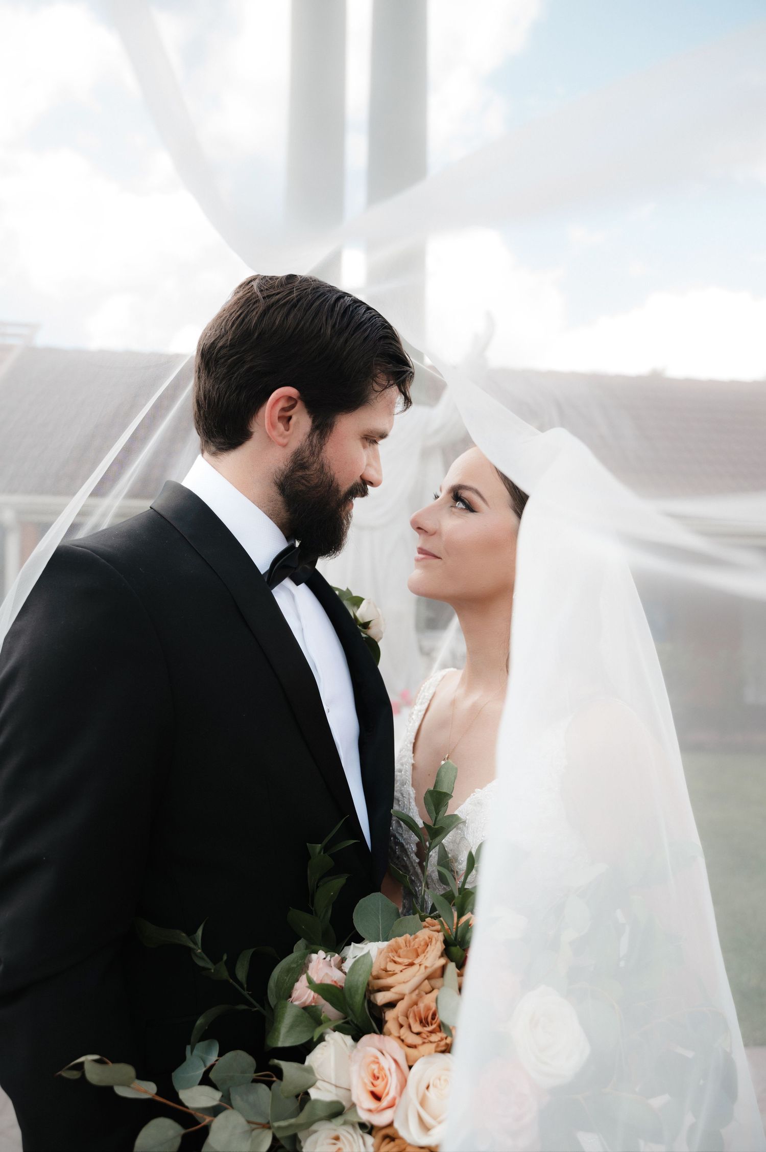 Romantic wedding portrait under veil with peach roses and greenery.