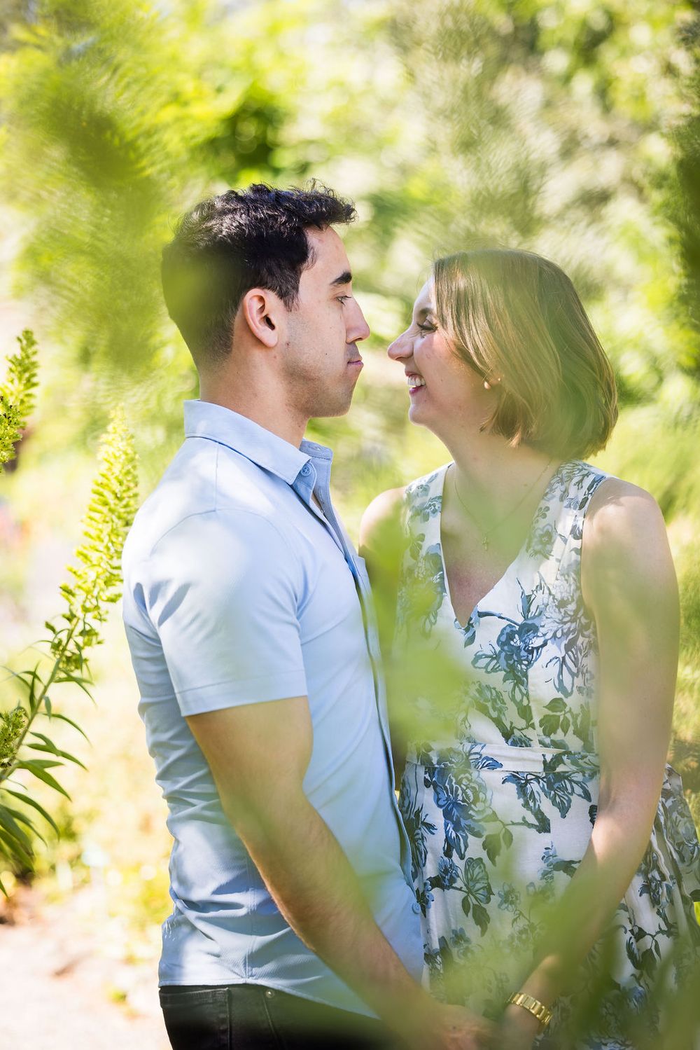Couple sharing a romantic moment surrounded by lush green garden foliage on a sunny day.