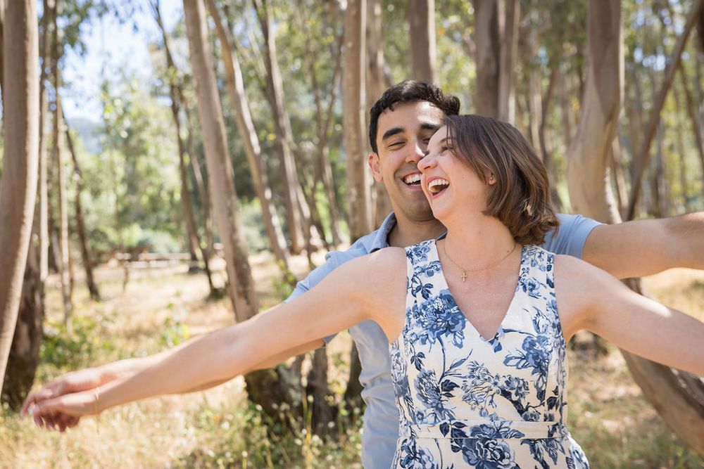 Joyful couple with arms outstretched embracing in a sunny eucalyptus forest.