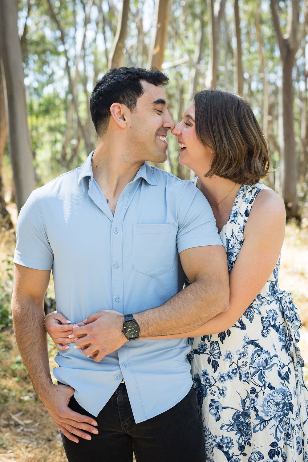 Happy couple smiling and embracing in eucalyptus forest during outdoor engagement session.