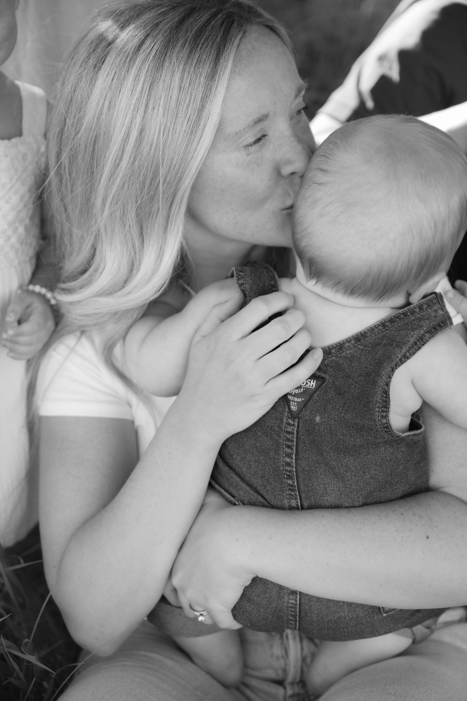 Candid photo of mom kissing baby boy's head during an outdoor spring lifestyle portrait session in Hudson, WI