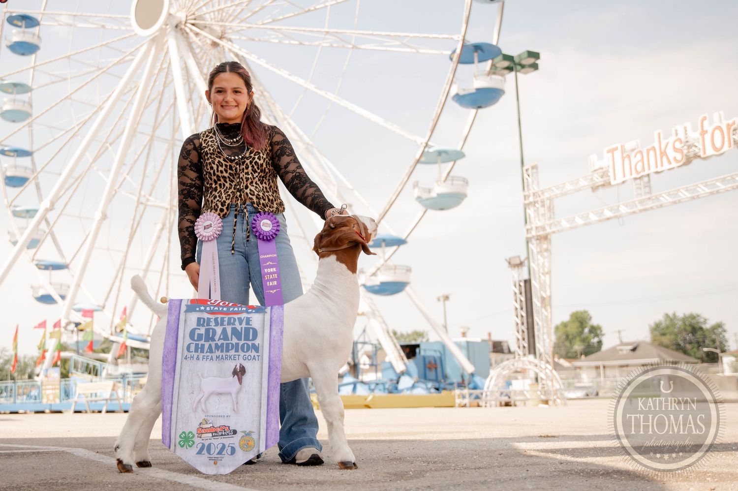 Young woman poses with her Grand Champion dog at a county fair, with a large Ferris wheel in the background.