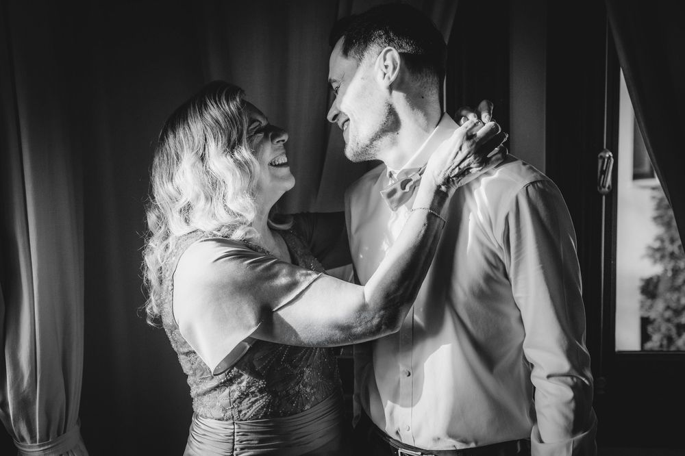 Black and white photo of a woman adjusting a mans bow tie, sharing a tender moment before a wedding ceremony.