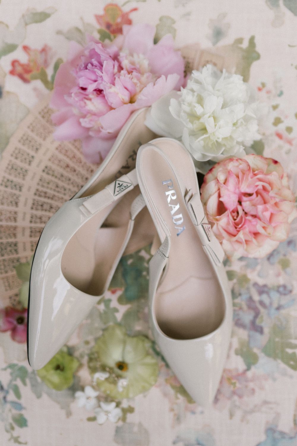 Elegant nude Prada patent leather heels displayed on floral background with pink and white peonies.