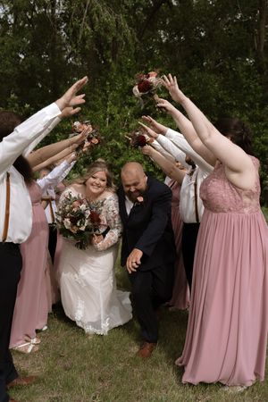 Bride and groom walk through an arch of raised hands formed by bridesmaids and groomsmen at outdoor wedding.