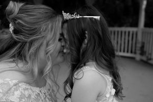 Bride wearing tiara shares tender moment with flower girl in black and white wedding photo.