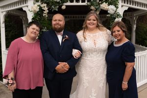 Bride and groom pose with two female family members near a white gazebo decorated with flowers.