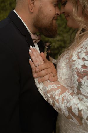 Close-up of bride and groom nearly kissing showing wedding rings on brides hands in lace gown.
