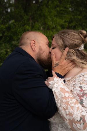 A bearded groom in navy suit shares a romantic kiss with his bride in lace wedding gown.