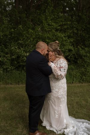 Bride and groom share an intimate forehead touch moment in a lush green outdoor wedding setting.