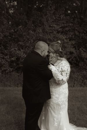 Black and white romantic photo of bride and groom sharing tender moment in outdoor garden setting.
