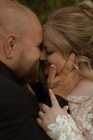 Intimate close-up of groom tenderly cupping bride's face as they touch foreheads, bride wearing lace gown.