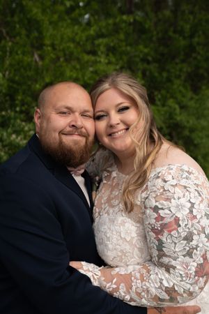 Happy bride and groom posing cheek to cheek smiling outdoors with green foliage background.