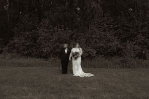 Black and white photo of a bride in white gown walking with a man in tuxedo across a lawn.