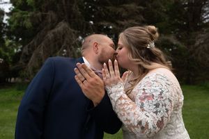 Bride and groom share a kiss outdoors with bride displaying her wedding ring prominently.