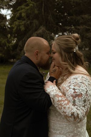 Bride and groom sharing intimate moment touching foreheads in lace wedding dress and black suit.