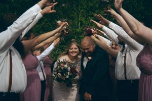 Newlyweds walk joyfully through a tunnel of raised arms formed by their wedding party.