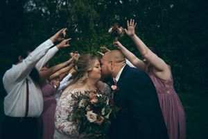 Wedding party raises hands as bride and groom share a kiss surrounded by bridesmaids and groomsmen.