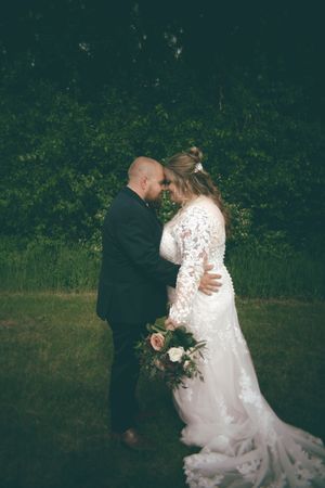 Bride and groom share a tender forehead-to-forehead moment in a lush green garden setting.