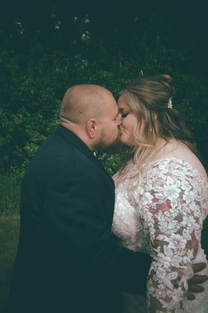 Bride and groom sharing first kiss outdoors in floral lace wedding dress and dark suit.