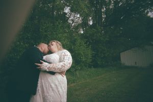 Bride and groom share a tender kiss outdoors surrounded by lush green trees at their wedding.